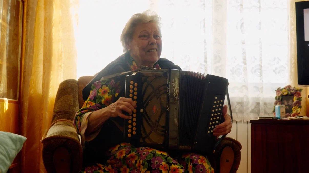 A woman playing an accordion beside a window
